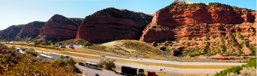 [Several photos stitched together. The canyon wall is a series of segmented cliffs rising hundreds of feet above the roadway. The road runs through a natural low point in this area.]